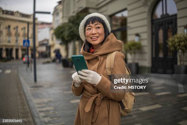 smiling japanese woman using mobile phone and waiting her friend on the street. - phone cover stock pictures, royalty-free photos & images