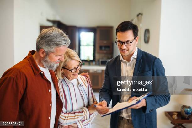 male real estate agent showing document to mature couple while talking with them - homeowners insurance stock pictures, royalty-free photos & images