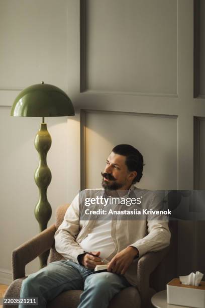 man relaxing in chair reading a book in cozy modern interior - efeito de luz imagens e fotografias de stock