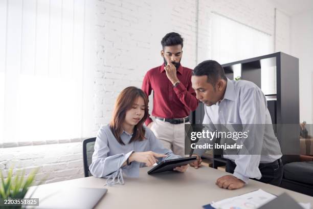 three people in a modern office collaborating on a project using a tablet while discussing ideas together - performance evaluation stock pictures, royalty-free photos & images