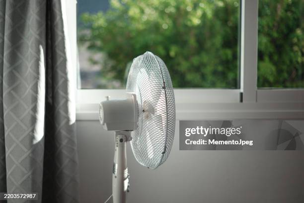 electric fan against window in bedroom at home, summer heat, air conditioning problems - ventilateur photos et images de collection