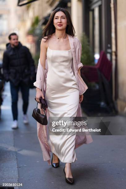 Guest wears silver necklace, shiny silk slip midi dress, light pink rolled up sleeve silk coat, shiny dark brown leather bag, shiny burgundy bordeaux...