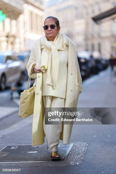Guest wears black sunglasses, gold pearl earrings, light pale yellow knit oversized sweater knotted around shoulders, light pale yellow oversized...