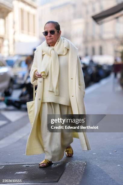 Guest wears black sunglasses, gold pearl earrings, light pale yellow knit oversized sweater knotted around shoulders, light pale yellow oversized...