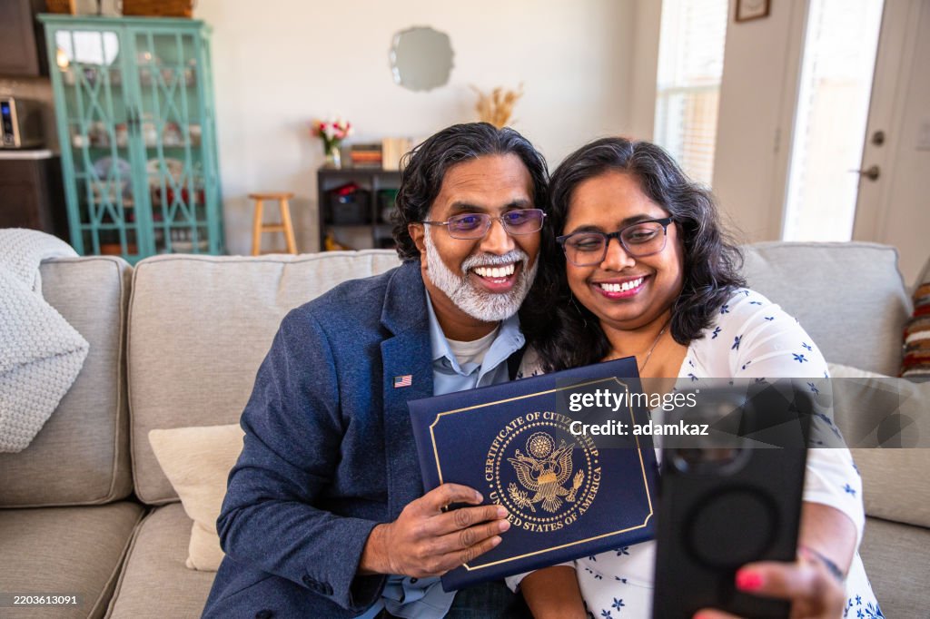 Proud Immigrant couple holding up their certifiicate of US Citizenship on a video call with family