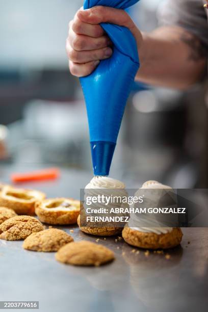 primer plano de un pastelero rellenando deliciosos hojaldres de crema con una manga pastelera, preparando un dulce en una cocina profesional - abastecedor fotografías e imágenes de stock