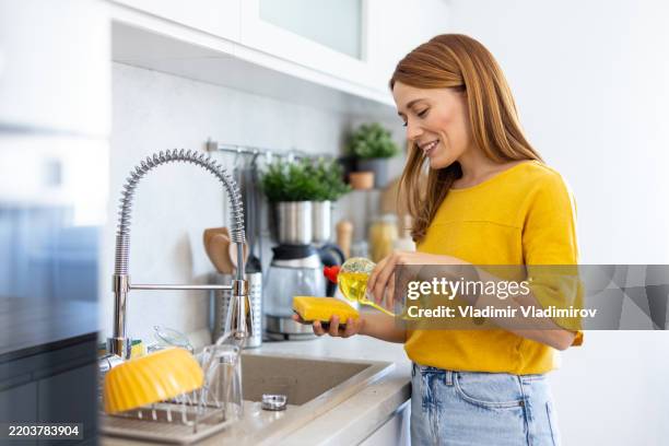 femme souriante versant de l’huile dans la cuisine avec joie - liquide vaisselle photos et images de collection