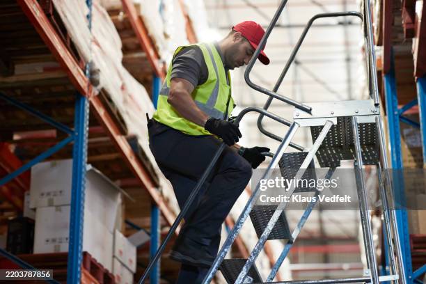 male worker climbing down ladder in warehouse - ladder stock pictures, royalty-free photos & images