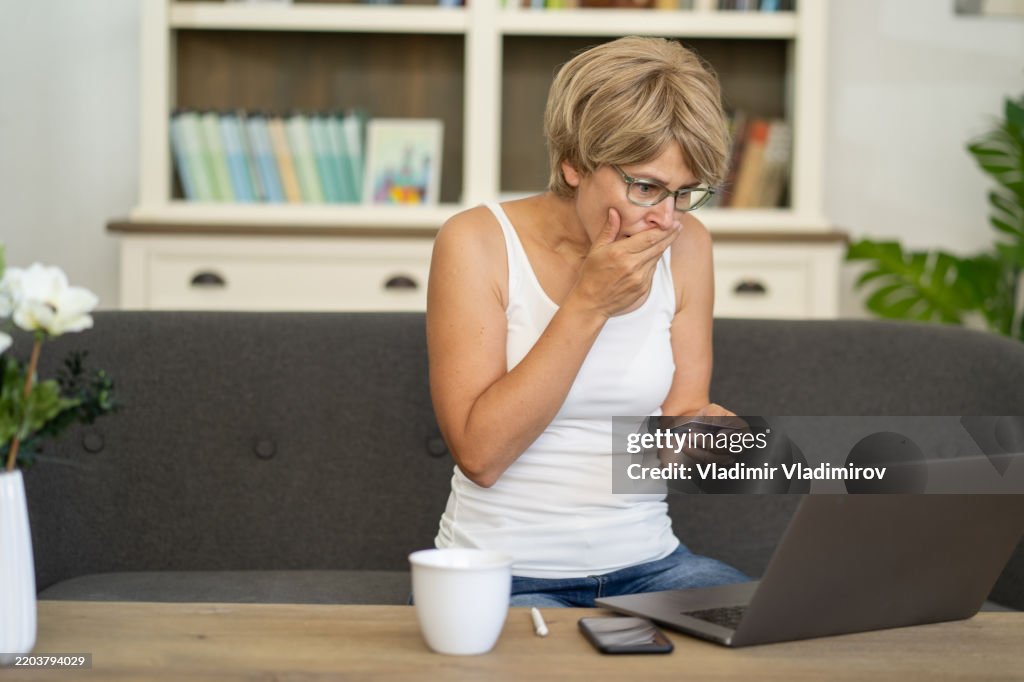 Concerned woman with a card at laptop focused on screen