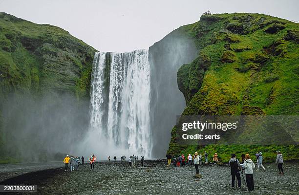 touristen, die den skogafoss-wasserfall in island bewundern - reiseroute golden circle stock-fotos und bilder