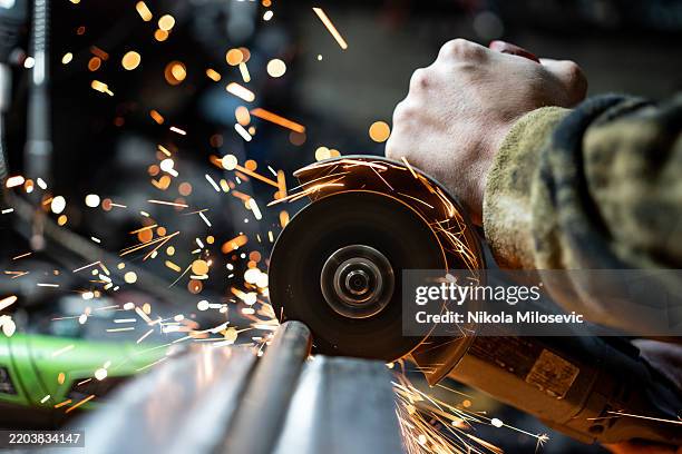 worker operating angle grinder with sparks flying during metal cutting - slijptol stockfoto's en -beelden