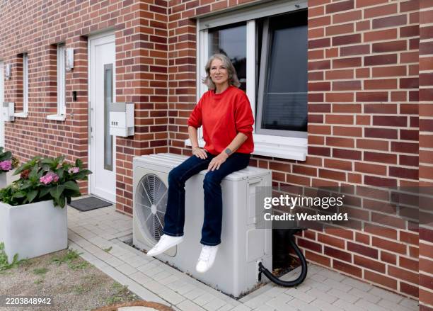 confident senior woman sitting on heat pump - wärmepumpe stock-fotos und bilder