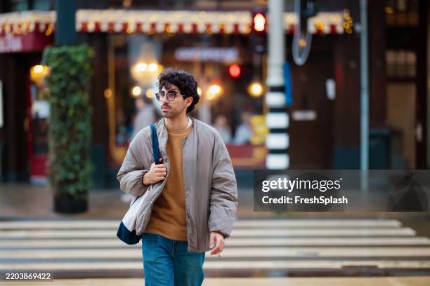 stylish man crossing street in urban setting with warm lighting - zebrapad stockfoto's en -beelden