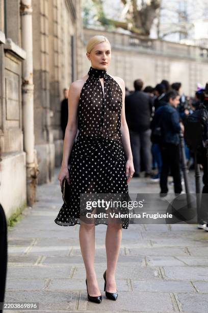 Guest wears a black leather bag, wears a see-through sleeveless black halter neck polka dots printed black and white midi dress and black pumps...