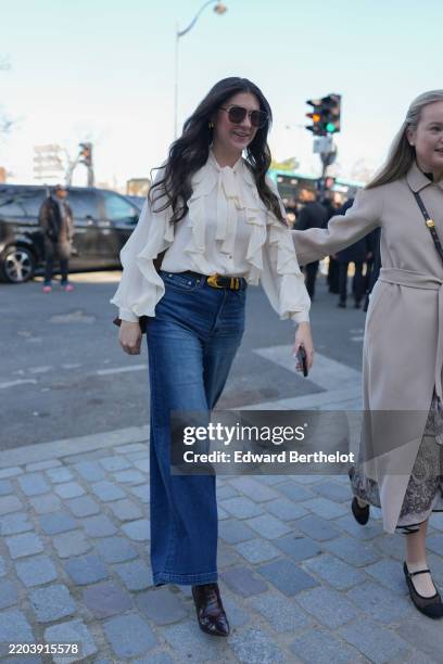Guest wears dark brown sunglasses, gold earrings, white sheer mesh flowy shirt, shiny black belt with gold buckle, navy blue washed loose denim jean...