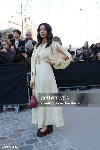Guest wears gold choker layered necklace, light pale yellow open sleeve midi dress, shiny burgundy bordeaux leather bag, black dark brown heeled mary...