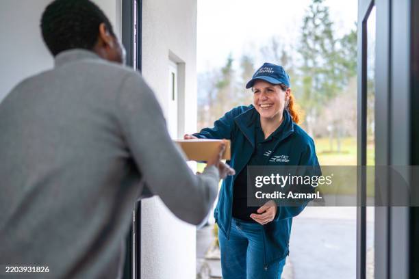 smiling delivery woman hands package to customer at doorstep - express delivery stock pictures, royalty-free photos & images