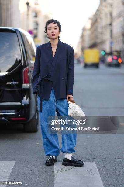 Mia Kong wears black pixie hair, gold hoop earrings, gold layered necklace, navy blue oversized Kenzo blazer jacket, navy blue baggy denim jean...