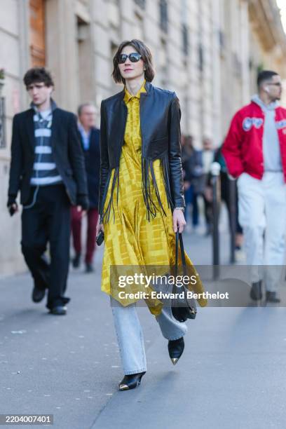 Guest wears black sunglasses, dark brown short hair, dark yellow pattern/print buttoned up long sleeve midi dress, shiny black cropped tassel leather...