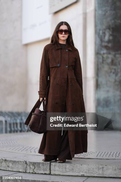 Guest wears dark brown sunglasses, dark brown sweater, dark brown double breasted suede trench coat, dark brown suede bag, gold rings, dark brown...