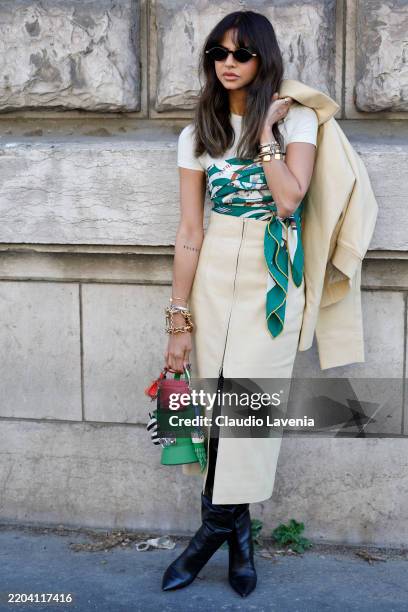 Guest wears white t-shirt, green white beige silk scarf as a top, cream leather midi skirt, black boots, pink and green Hermes bags, outside Hermès,...