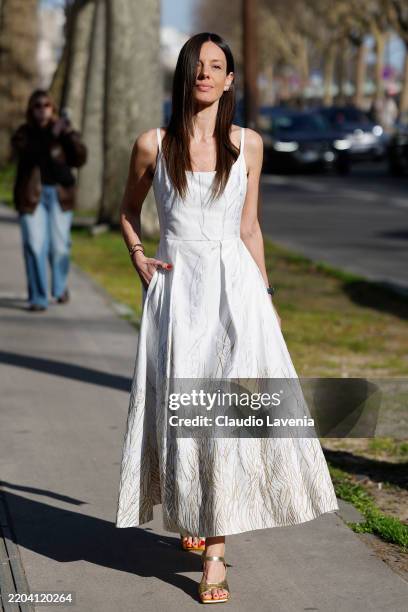 Guest wears white maxi dress with silver and gold decorations, black mini bag, gold heels, outside Elie Saab, during the Womenswear Fall/Winter...