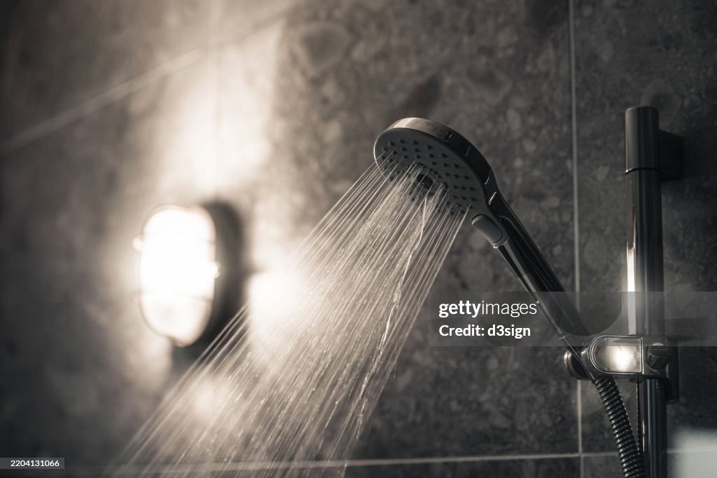 Close-up of water flowing from shower head in a modern, stylish bathroom interior with grey wall tiles. Home interior. Ready for a refreshing shower