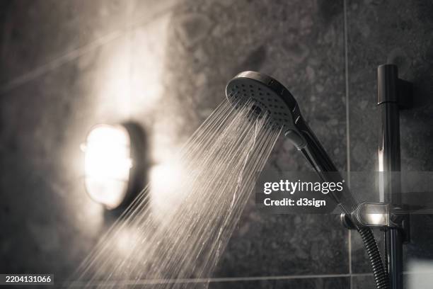 close-up of water flowing from shower head in a modern, stylish bathroom interior with grey wall tiles. home interior. ready for a refreshing shower - douche stockfoto's en -beelden