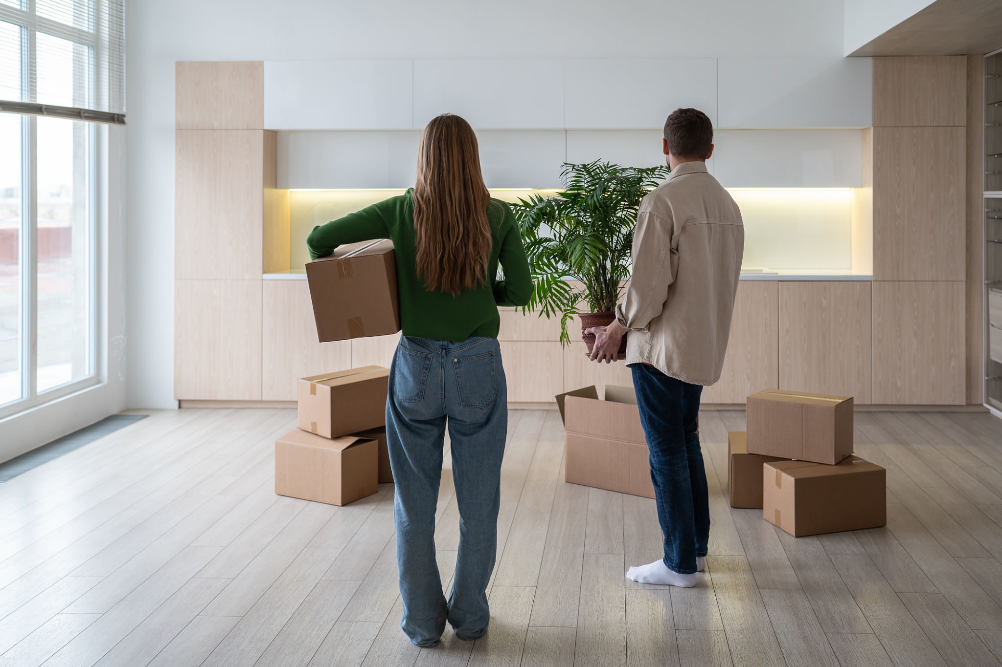 New home owners with boxes and houseplant in hands. Housewarming relocation in mortgage apartment. New home owners with boxes and houseplant in hands. Housewarming relocation in mortgage apartment.