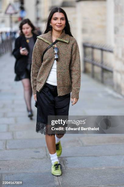 Guest wears silver earrings, dark brown pattern oversized unzipped cardigan jacket, white top, black sunglasses in top, shiny black crossbody leather...