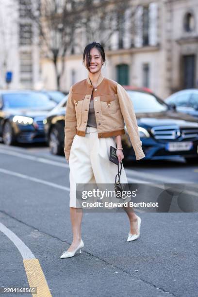 Jihoon Kim wears light brown Hermès leather jacket, white higj waisted loose trouser pants, gold watch, black small leather bag, white pointed toe...