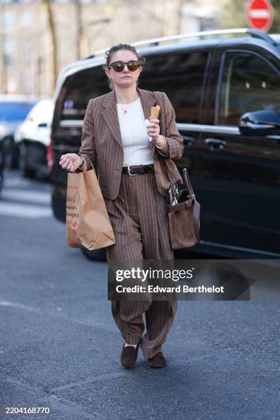 Guest wears dark brown sunglasses, cream shirt, gold necklace, dark brown white pinstripe blazer jacket, shiny dark brown leather belt, dark brown...