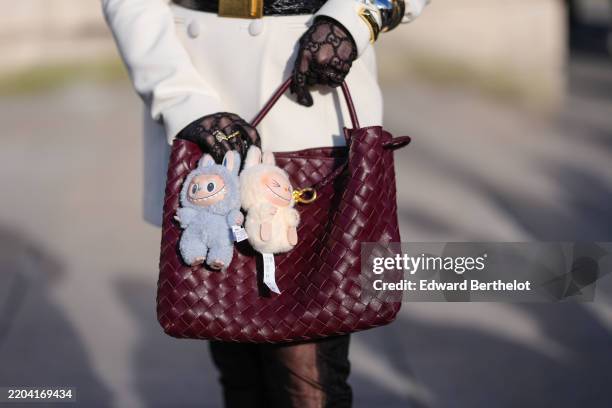 Guest wears a burgundy bordeaux woven Bottega Veneta Andiamo leather bag, light blue Labubu bag charm, cream Labubu bag charm, outside Elie Saab,...
