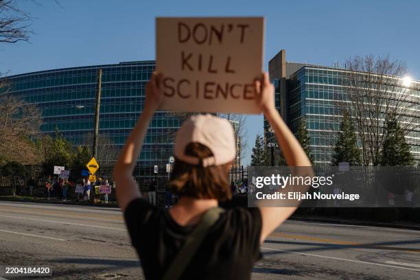 People protesting personnel cuts at the Centers for Disease Control hold signs outside the organization's main headquarters on March 12, 2025 in...