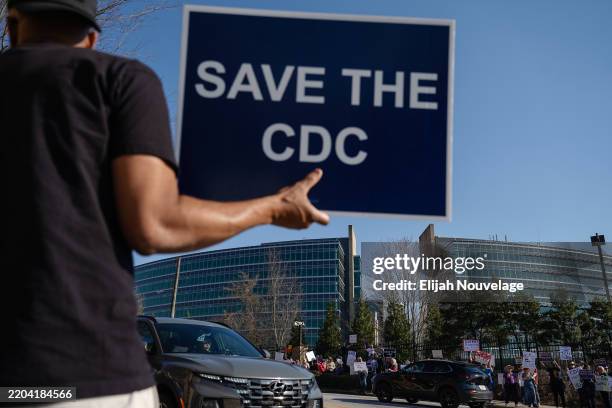 People protesting personnel cuts at the Centers for Disease Control hold signs outside the organization's main headquarters on March 12, 2025 in...