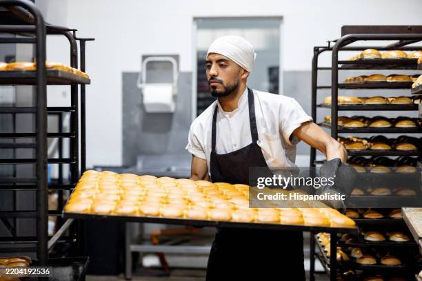 baker moving a tray of bread out of the over at an industrial bakery - appliance manufacturing stock pictures, royalty-free photos & images