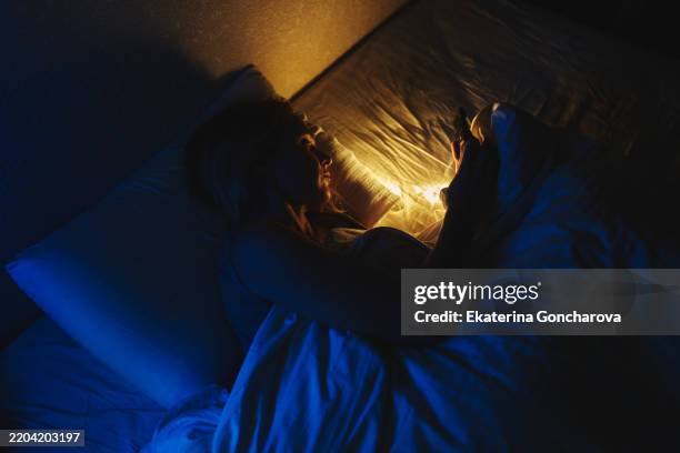 woman using a smartphone at night in a dimly lit bedroom. insomnia - ambient light stock pictures, royalty-free photos & images