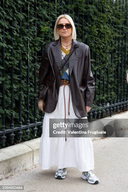 Guest wears brown sunglasses, a brown leather jacket, a mustard yellow, green and blue knitted sweater, a brown belt, a white high waist skirt and...