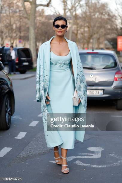 Guest wears light blue long dress with flower decorations, light blue coat, silver heels, white bag, outside Georges Hobeika, during the Womenswear...