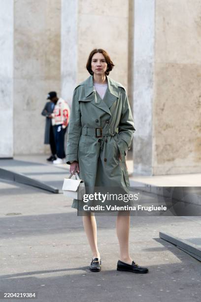 Guest wears black leather loafers, a white leather bag, a green trench with a cut-out detail on the back and a white mini dress outside Niccolò...