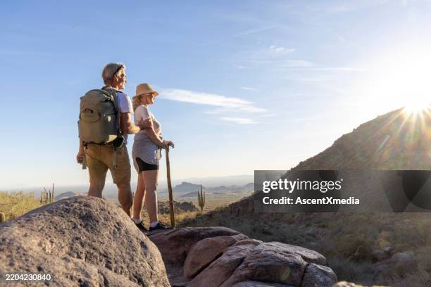 reifes wanderpaar steht bei sonnenuntergang auf einem felsen über der wüste - vorruhestand stock-fotos und bilder