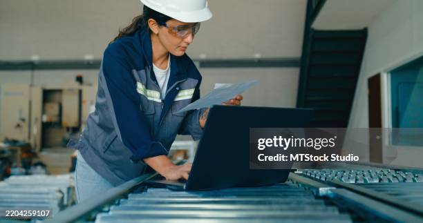 young female engineer wearing hardhat uses laptop to analyze data and manage operations in factory. robotic industrial factory. - rpa stock pictures, royalty-free photos & images