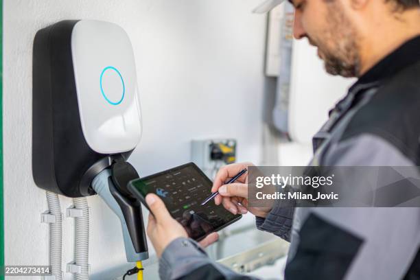 un ingénieur utilise une tablette numérique pour examiner la station de recharge d’une voiture électrique - chargeur de batterie photos et images de collection