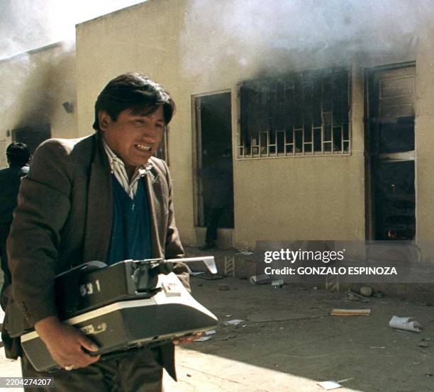 An employee of Alcaldia in El Alto of La Paz takes a typewriter that he rescued from the fire 29 May, 2000 caused by the protesting students and...