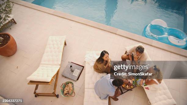 verschiedene freunde, die an einem sonnigen tag wein und wurstwaren an einem entspannenden pool genießen - schwimmbeckenrand stock-fotos und bilder