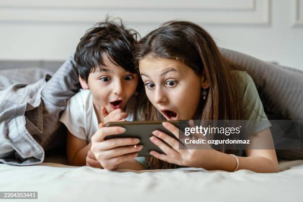 children watching cartoon in bed with a surprised expression on their faces - verbazing stockfoto's en -beelden