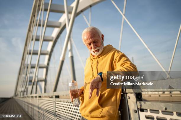 senior man checking smartwatch during fitness exercise on bridge - durability stock pictures, royalty-free photos & images