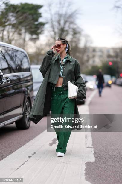 Guest wears dark brown sunglasses, gold earrings, dark green white striped buttoned up long sleeve cropped shirt, dark green Lacoste jacket, dark...