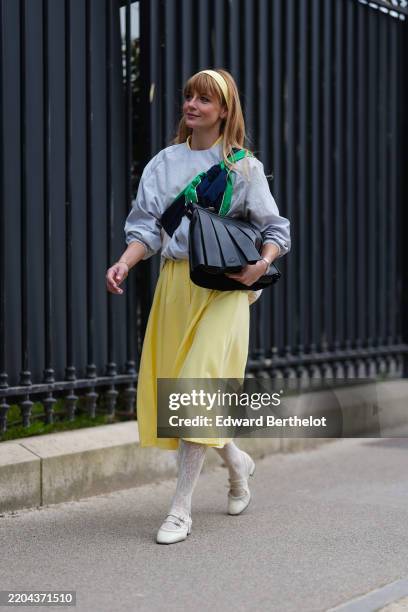 Mafalda Patrício wears bright yellow headband, light gray oversized jacket, navy blue around the shoulder sweater, shiny black Lacoste leather bag, a...