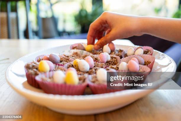 hand putting decorations on to easter cup cakes in dish on kitchen table - easter cupcake stock pictures, royalty-free photos & images
